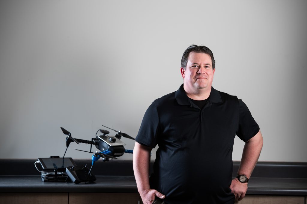 Jeremy Laliberté stands leaning against a counter next to a UAV.