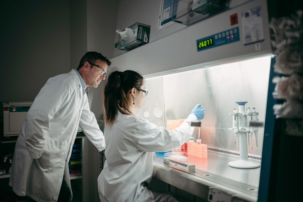 Two researchers in lab coats, one holds a test dropper