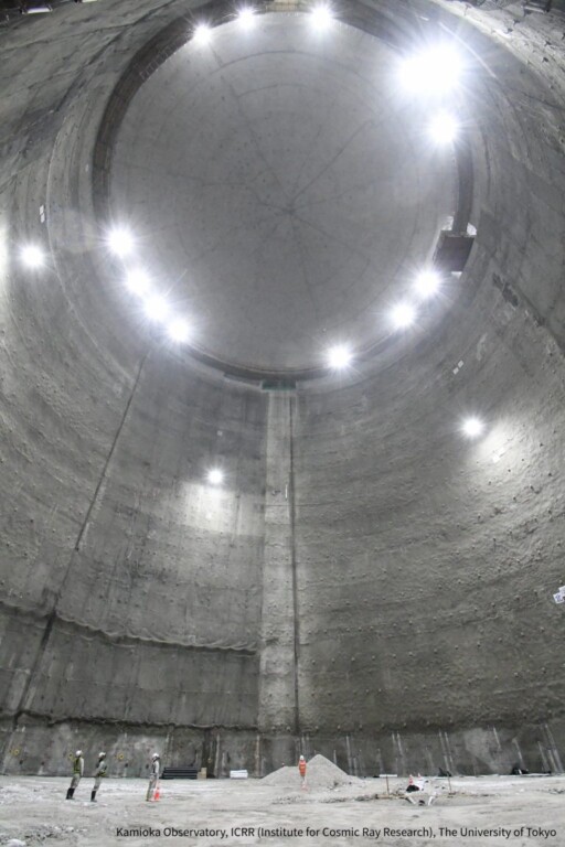 Large empty interior of a dome-shaped excavated cavern. Three people on the ground looking up.