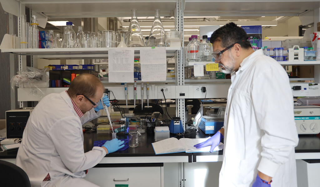 Aguilar-Valles and a team member at work in the lab inserting a sample into a test tube.