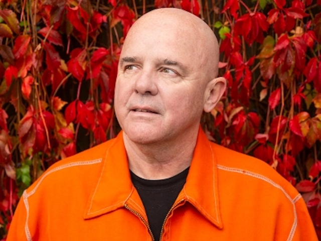 Head shot of a man in an orange shirt with red leaves backdrop